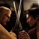 Two men attack each other with swords while staring at each other menacingly.